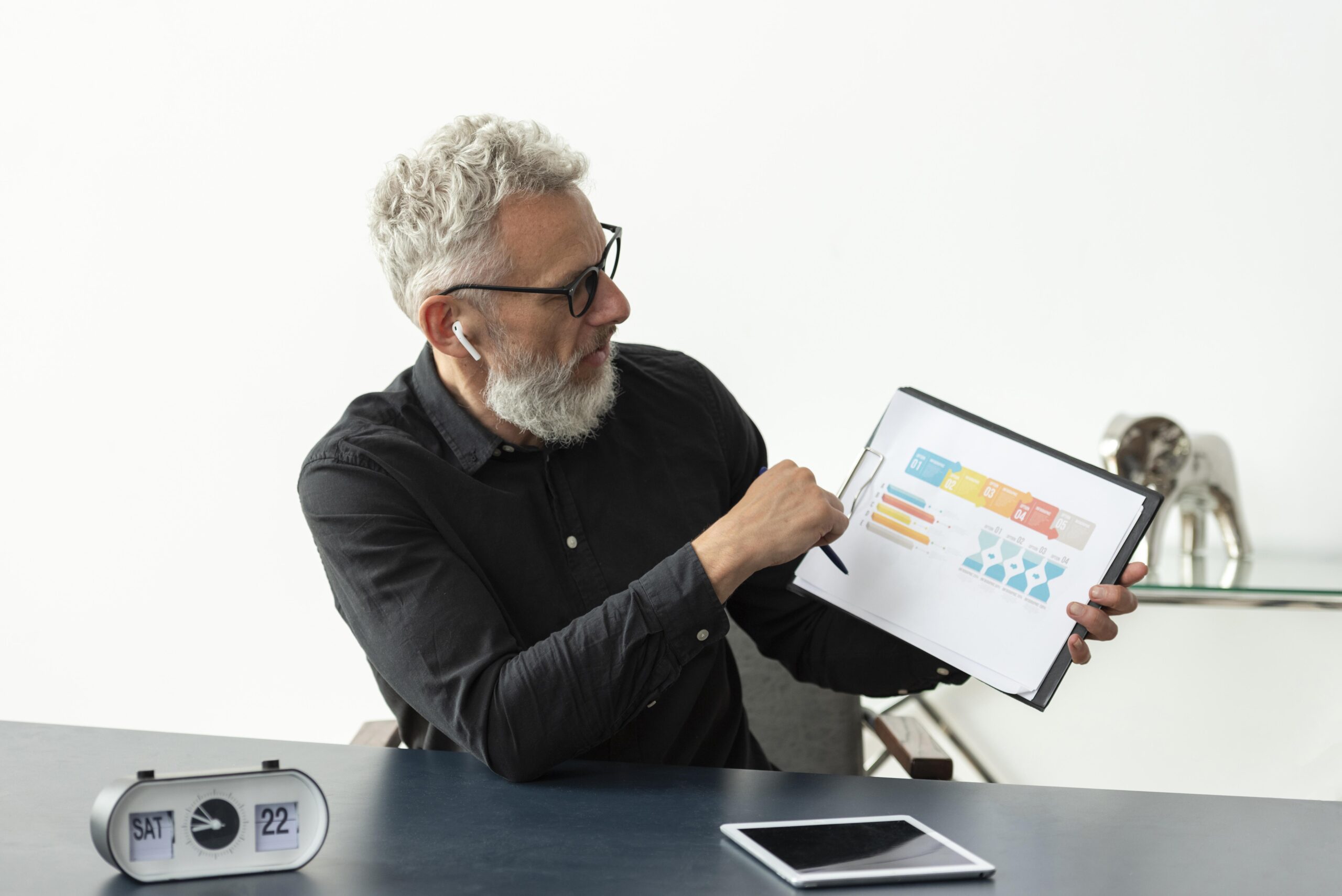 older-man-home-showing-graph-notepad-with-tablet-desk