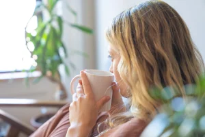 Mujer sentada con una taza en las manos, pensativa, en un momento de calma en casa