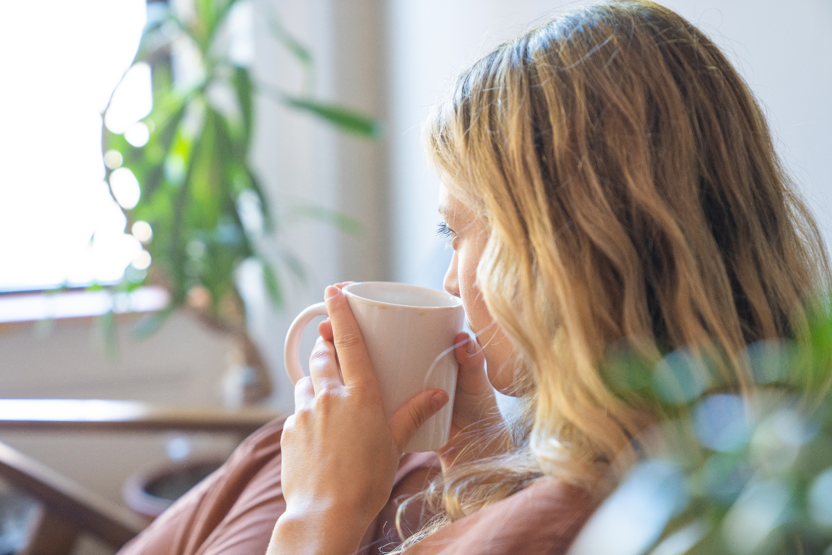 Mujer sentada con una taza en las manos, pensativa, en un momento de calma en casa