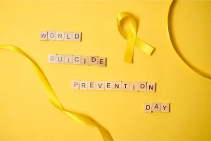 : Lazo amarillo sobre fondo amarillo y piezas de madera que forman la frase “World Suicide Prevention Day”
