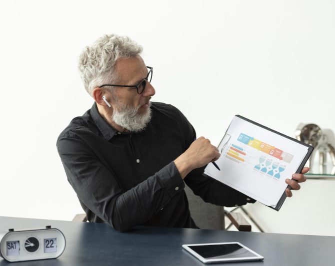 older-man-home-showing-graph-notepad-with-tablet-desk